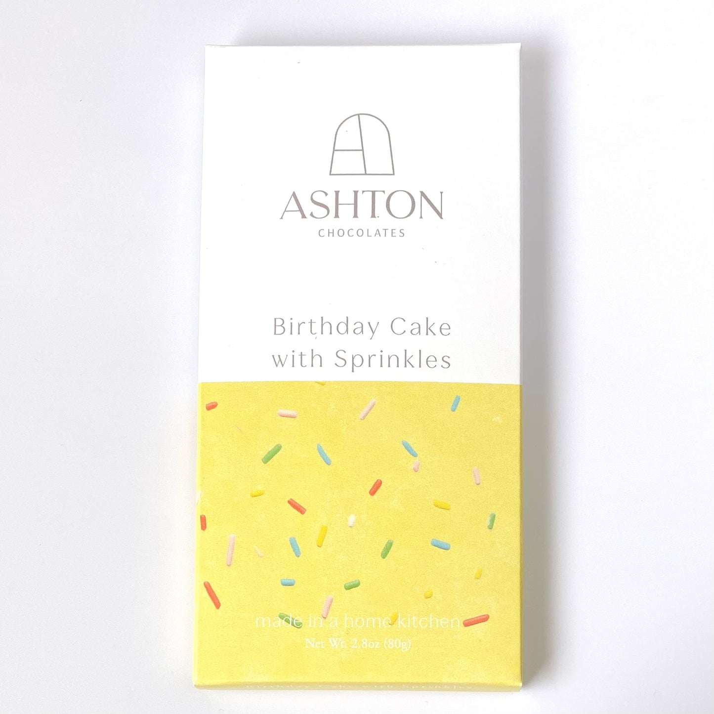 A Birthday Cake with Sprinkles chocolate bar box. Half of the box is white the other half is yellow with rainbow sprinkles.